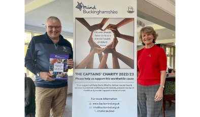 A man and a woman stand either side of a pop-up display banner promoting Buckinghamshire Mind as the The Captains' Charity 2022/23