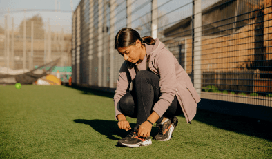 A young woman crouching down to tie the shoelace of her trainers.