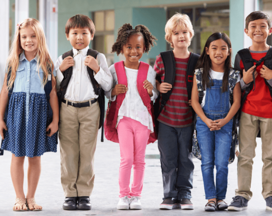 A diverse group of Primary School age children, standing in a line and smiling. They're wearing non-uniform.