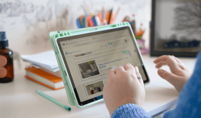 A tablet on a desk. The hands of someone using the table are visible.