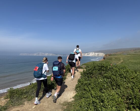 A group of people shown from behind walking along a clifftop coastal path.