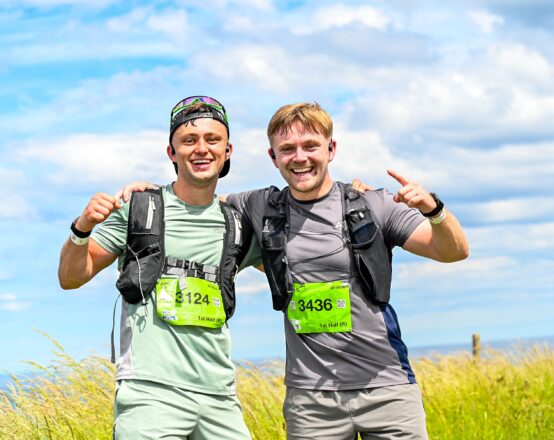 Two male competitors standing arm and arm, smiling. They are in a field with blue sky in the background.