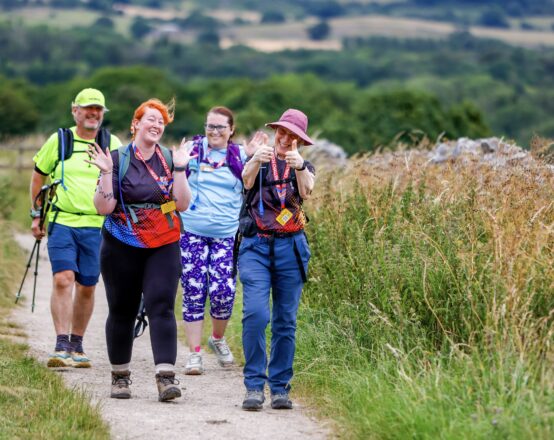A group of four walkers who are smiling and walking along a path through a field in the countryside.