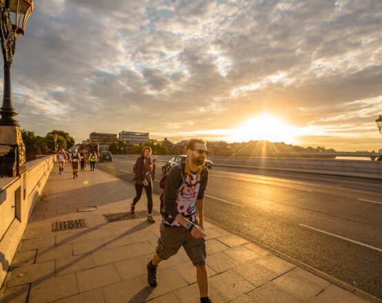 People walking across a bridge in London as the sun sets